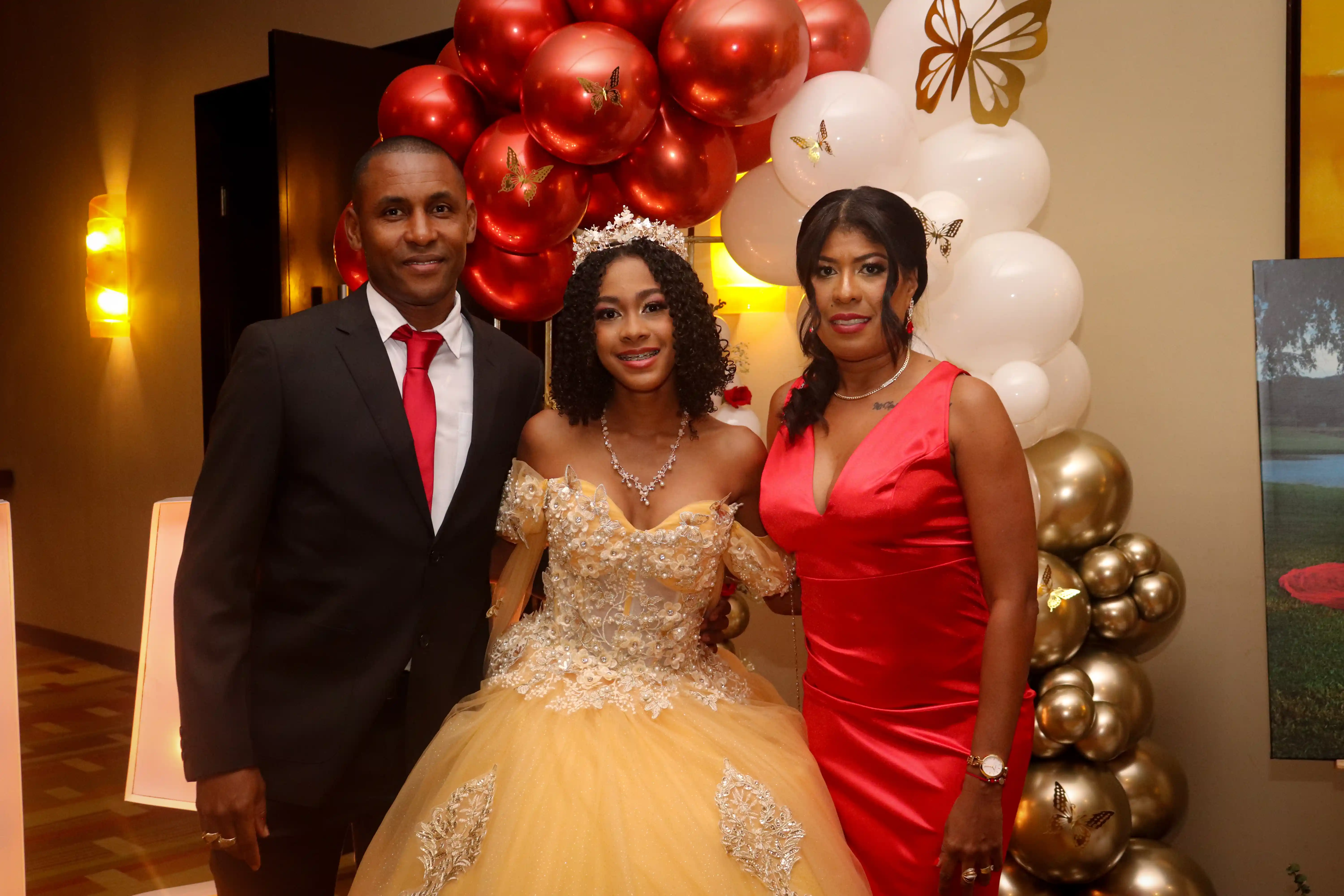 Quinceañera sonriente posando en su elegante vestido junto a sus padres en su celebración