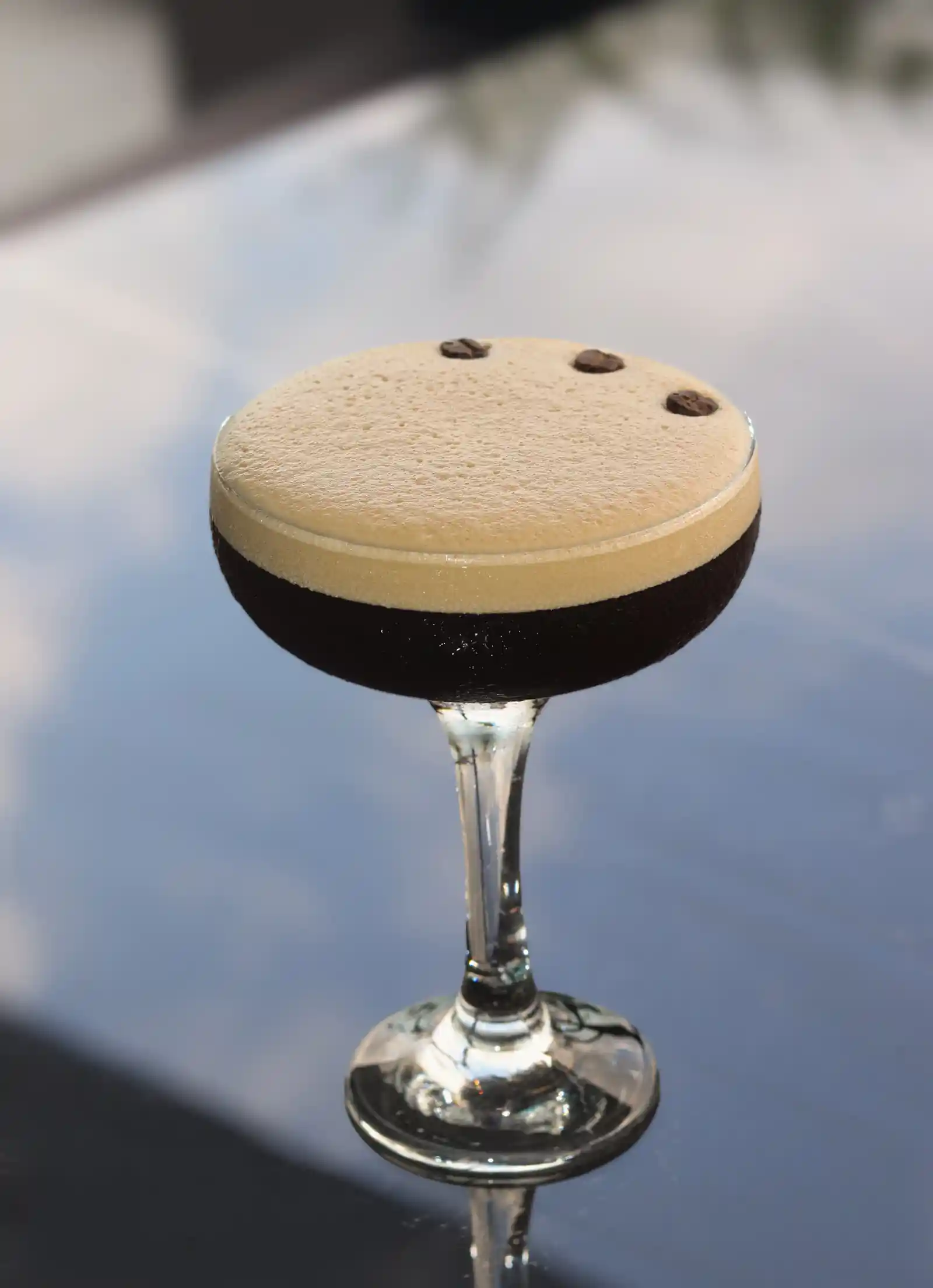 Un rico martini de espresso con espuma cremosa y granos de café, servido en una elegante mesa de cristal
